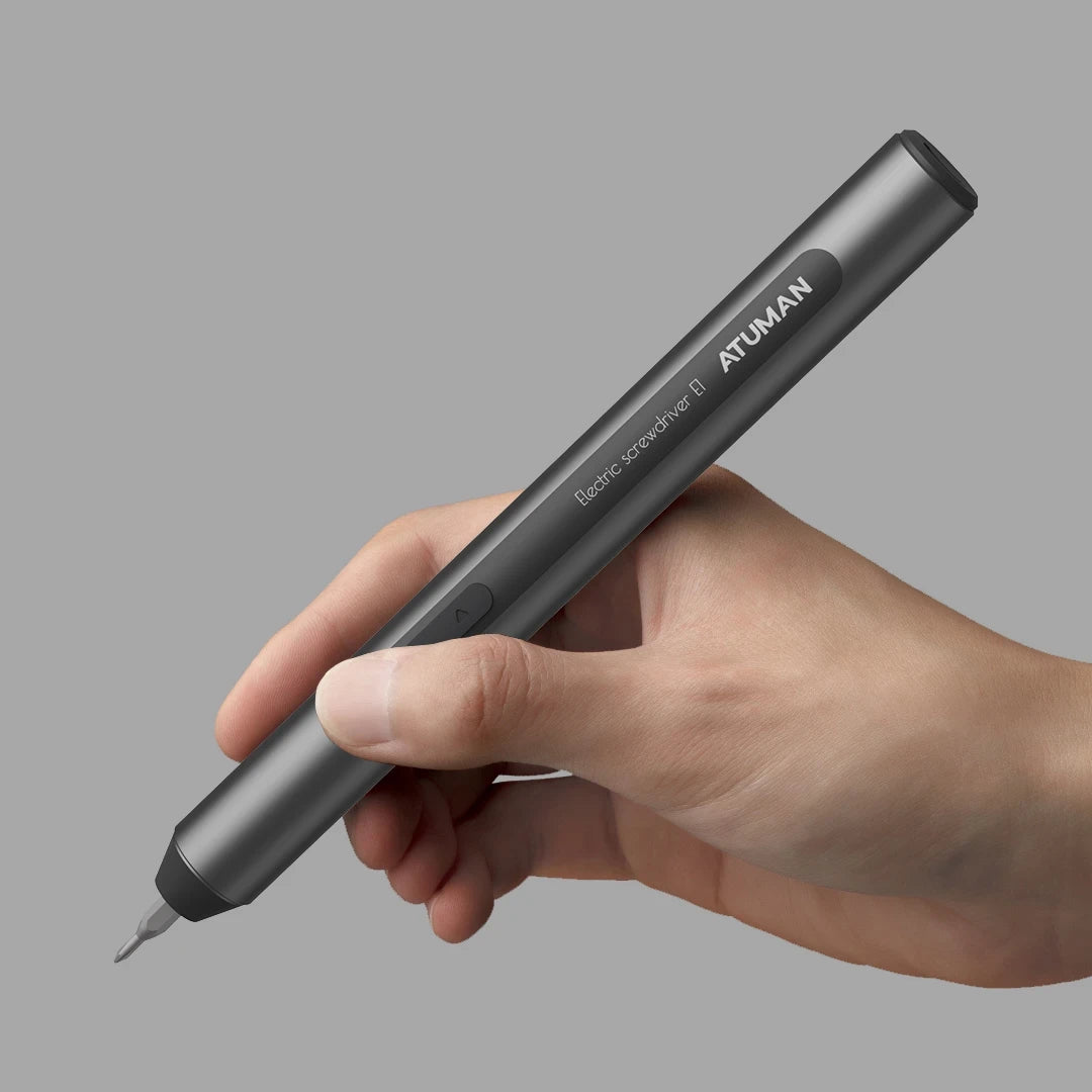 A hand holding a black, pen-shaped electric screwdriver branded with "ATuMan." The tool is sleek and modern, designed for precision tasks, and features a bit at the tip. The label on the tool reads "Electric Screwdriver ATuMan." The background is gray, highlighting the tool and hand.