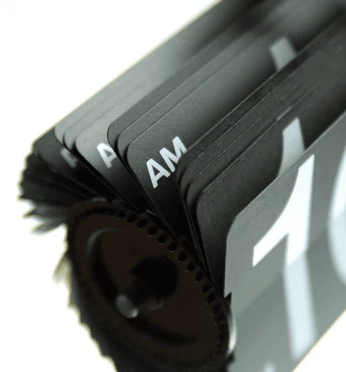 A close-up view of the flip cards mechanism inside a vintage-style flip clock. The image focuses on the black flip cards stacked together, with "AM" and part of a number visible on the cards. The gears and inner workings of the clock mechanism are also partially visible, highlighting the intricate design and engineering of the flip clock.