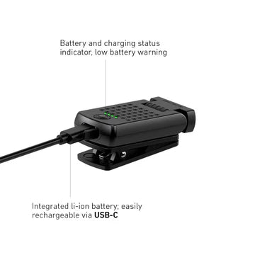 A compact black LED clip light with a long, narrow LED strip at the front is shown being charged via a USB-C cable. The text highlights the light's features, stating "Battery and charging status indicator, low battery warning" and "Integrated li-ion battery; easily rechargeable via USB-C." The image demonstrates the light's rechargeable capability and the convenience of the charging status indicator.