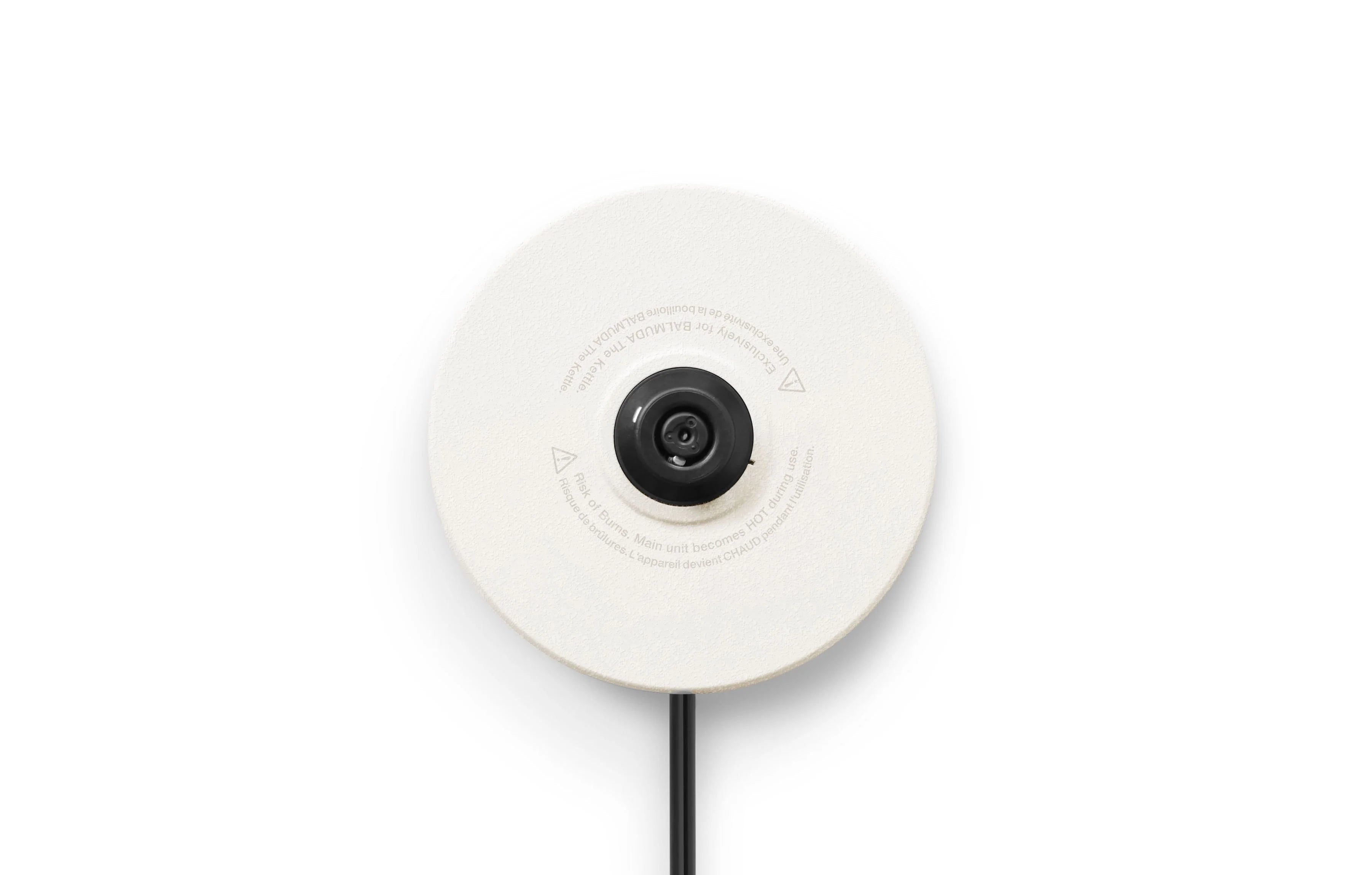 The image shows a close-up view of the underside of a circular white base, likely the base of a kitchen appliance or a charging stand. At the center, there is a black connector or plug surrounded by printed text that includes safety warnings and usage instructions. A black cord extends downward from the center of the base.