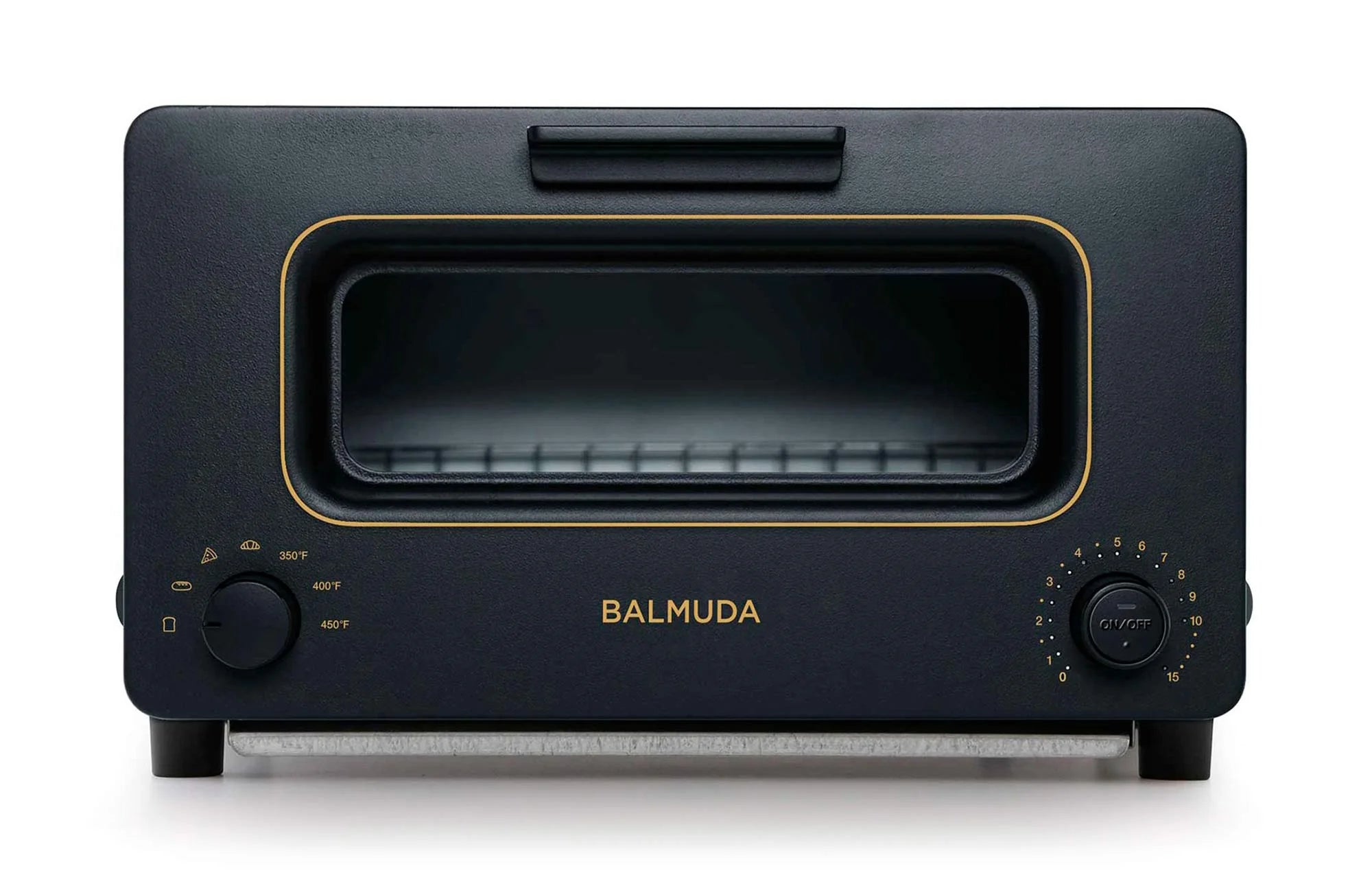 The image shows a front view of a Balmuda toaster in a matte black finish with gold accents. The toaster features a large rectangular viewing window centered on the front, bordered by a gold trim. Below the window, the brand name "BALMUDA" is prominently displayed in gold lettering