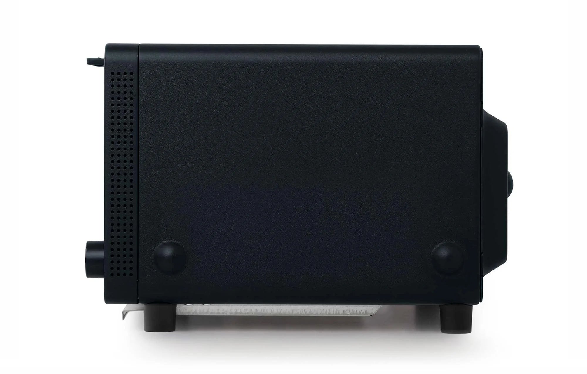 The image shows a side view of a Balmuda toaster in a matte black finish. The side panel is smooth and minimalist, with two small circular feet near the bottom for stability. Toward the front, there is a series of small ventilation holes arranged in a vertical line, providing airflow to the interior components