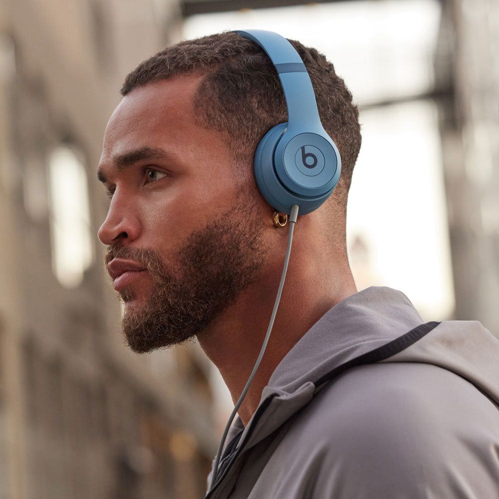 "Man wearing blue Beats by Dre wireless over-ear headphones in an urban setting, highlighting modern design and immersive sound quality."