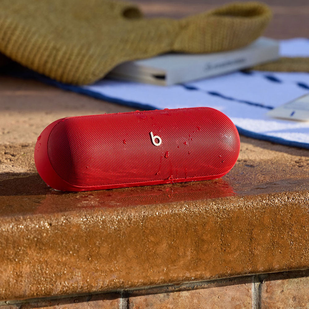 For the image you just uploaded, here is an alt text suggestion:
A red Beats portable speaker with water droplets on its surface, placed by a poolside, highlighting its water-resistant feature. A towel and a book in the background emphasize its suitability for outdoor use.