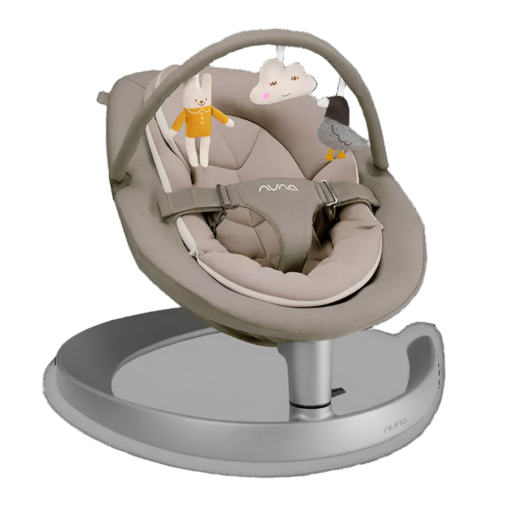 A beige baby rocker with a soft cushioned seat and a toy bar featuring a bunny, cloud, and bird plush toys, mounted on a sleek silver circular base.