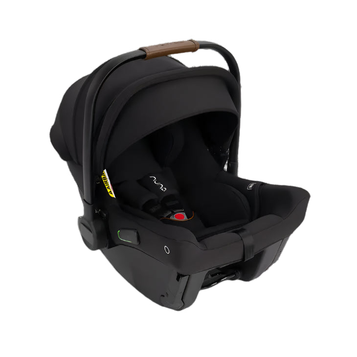 Front angled view of a black Nuna infant car seat featuring a leatherette handle, extended canopy, and a visible five-point harness with a red buckle. The car seat rests on its base, showing part of the recline adjustment mechanism.