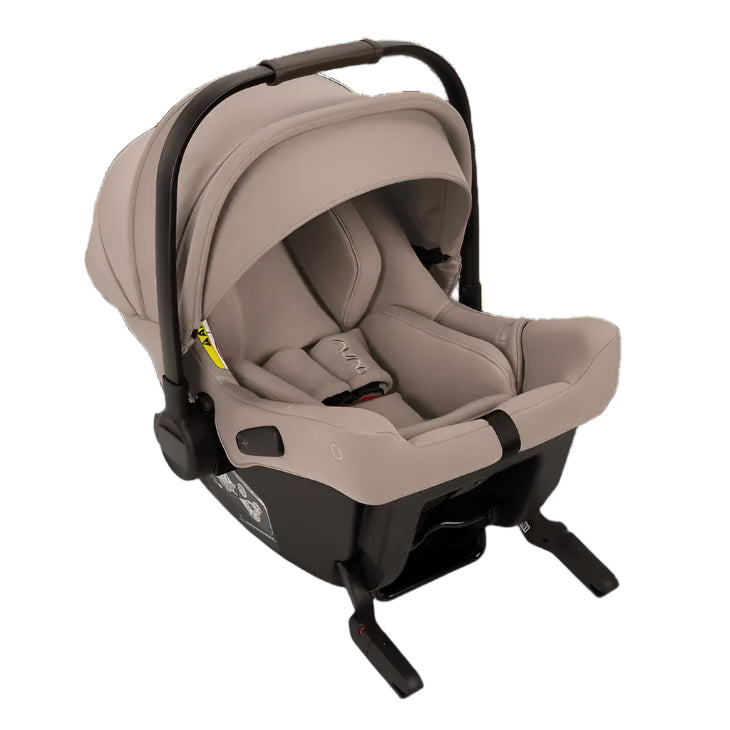 A beige Nuna infant car seat with a canopy and five-point harness is shown from a front angle, securely attached to a base with Isofix connectors for safe vehicle installation.
