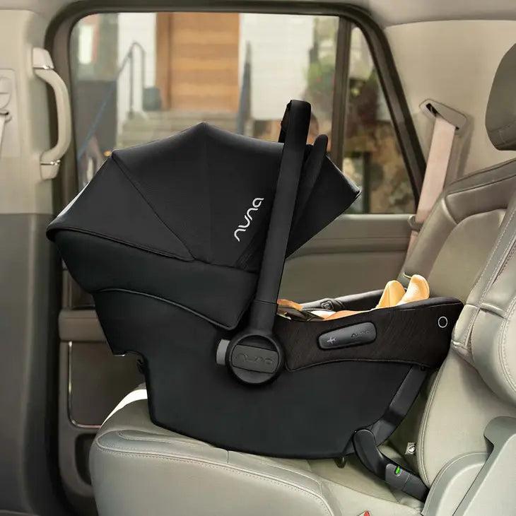 A black Nuna infant car seat is securely installed rear-facing on a vehicle seat, with its canopy extended and ergonomic carry handle upright, showcasing a sleek design and safety-focused build.