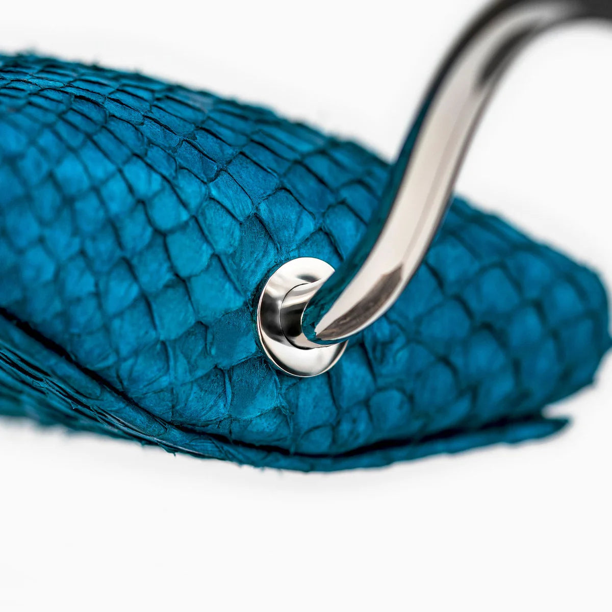 A close-up view of a blue textured cushion attached to a shiny, curved metal support. The cushion has a scaly, reptile-like texture, and the metal support is secured with a polished metal screw. The image highlights the luxurious materials and the detailed