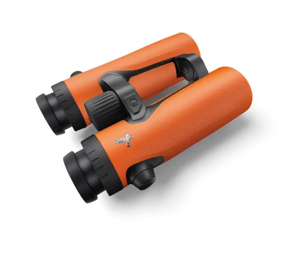 A dynamic angle of Swarovski Optik bright orange binoculars, showcasing their rugged texture, ergonomic design, and iconic Swarovski bird logo on the barrel.