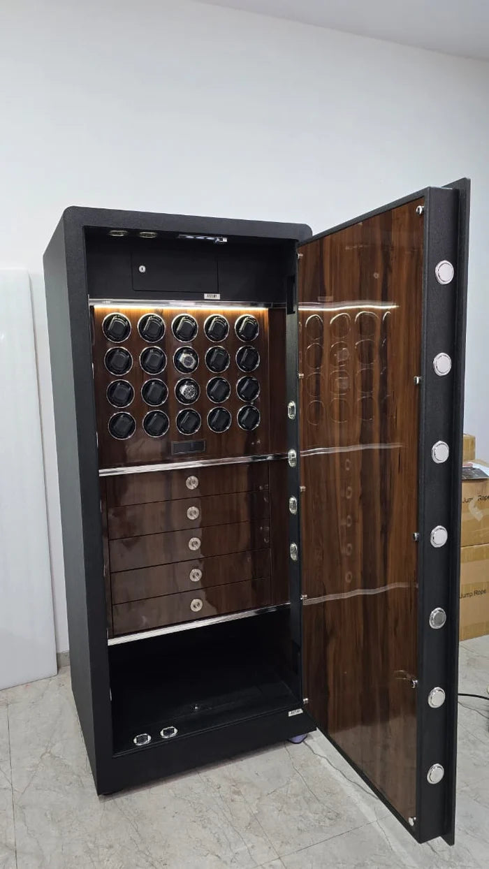 A large, open safe with a dark exterior and wooden interior is shown. The interior features multiple compartments, including three large drawers at the bottom and two rows of watch holders above them. The door of the safe is open, revealing the well-organized storage system designed for watches and other valuables.