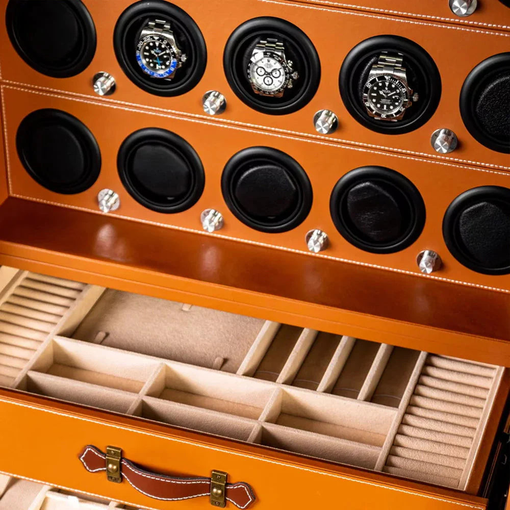 Close-up view of a safe's interior featuring an orange leather finish. The top section has watch winders with several luxury watches displayed. Below the watch winders is an open drawer with multiple compartments lined with soft material for organized storage of watches and other small items. The design emphasizes both functionality and elegance.