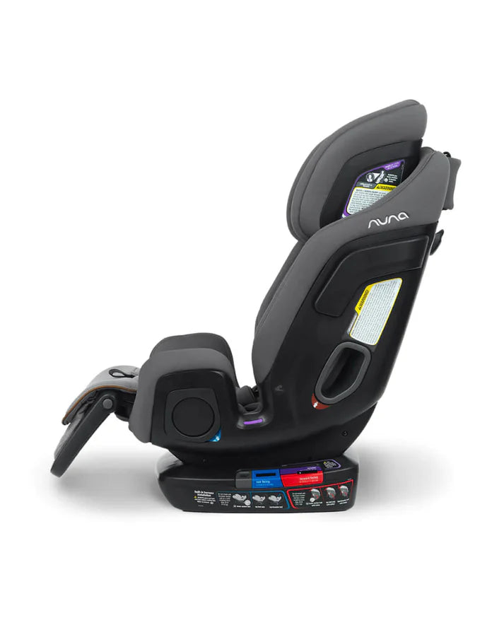 Side view of a Nuna child car seat in grey showing the adjustable recline feature, belt path indicators for rear and forward-facing installation, and clear safety labels.