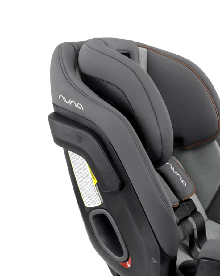Close-up of the Nuna convertible car seat in grey, highlighting the padded headrest, side impact protection pod, and the harness system with visible branding.
