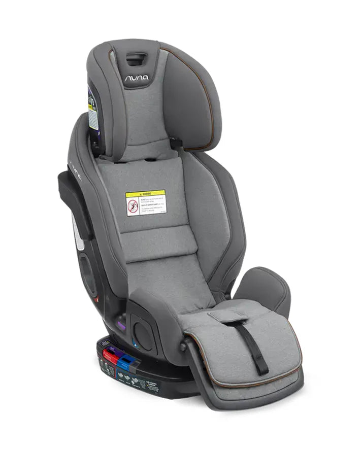 A grey Nuna convertible car seat in booster mode, featuring a high backrest, extended leg rest, no harness straps, and clear safety labeling on the seat.