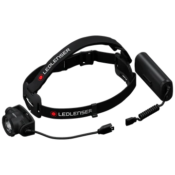 A disassembled view of a black LED Lenser headlamp, showing the adjustable strap with the LED Lenser logo, the detachable headlamp unit, and the battery pack connected by a coiled cable. The components are laid out on a white background, highlighting the headlamp's modular design and ease of assembly.