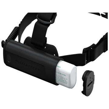 A black LED Lenser headlamp with an adjustable strap, shown with the battery compartment open. The battery pack is partially pulled out, revealing a cylindrical battery. The cap of the battery compartment is placed beside it. The LED Lenser logo is visible on the strap. The background is white, emphasizing the details of the headlamp and its components.