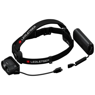 An LED Lenser headlamp with its components separated. The adjustable black strap with the "LED LENSER" branding is connected to the light unit, which features dual lenses. The battery pack is shown separately with a coiled cable ready to be connected to the light unit. The image highlights the modular design of the headlamp for easy assembly and battery replacement.