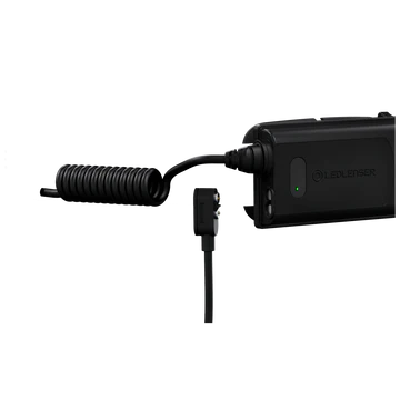 A close-up view of the black LED Lenser headlamp's battery pack and its connecting coiled cable. The battery pack features a green LED indicator showing the charge level. The background is white, highlighting the details of the battery pack and the coiled cable connection.