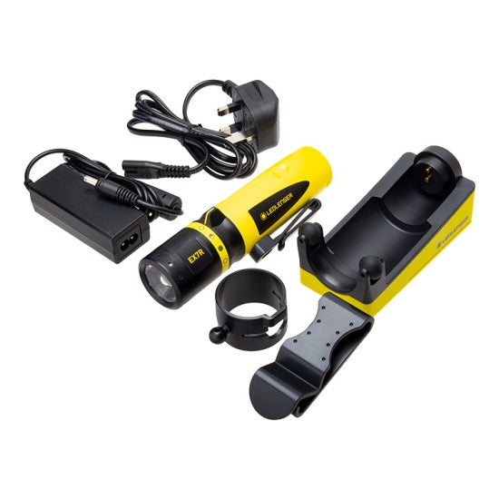 The LEDLenser EX7R flashlight set, including the yellow and black flashlight, a yellow docking station, various attachments, and charging cables with a plug adapter. The components are arranged neatly for display.