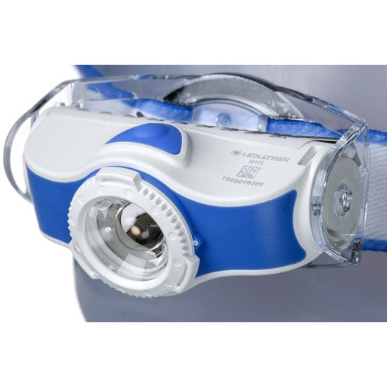 A close-up view of a white and blue LED Lenser headlamp. The headlamp features a clear central lens and an adjustable strap. The LED Lenser branding is visible on the side of the unit. The design is ergonomic and modern, suitable for hands-free illumination.