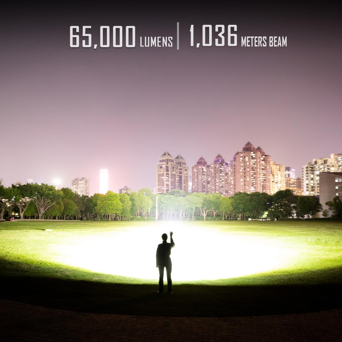 Promotional image demonstrating the power of the IMALENT MS12 MINI flashlight. A person stands in the middle of a large, illuminated area at night, holding the flashlight and pointing it forward. The beam is so intense that it lights up the entire field, with buildings and trees visible in the background. The text at the top reads "65,000 Lumens | 1,036 Meters Beam," showcasing the flashlight's impressive brightness and long beam distance.