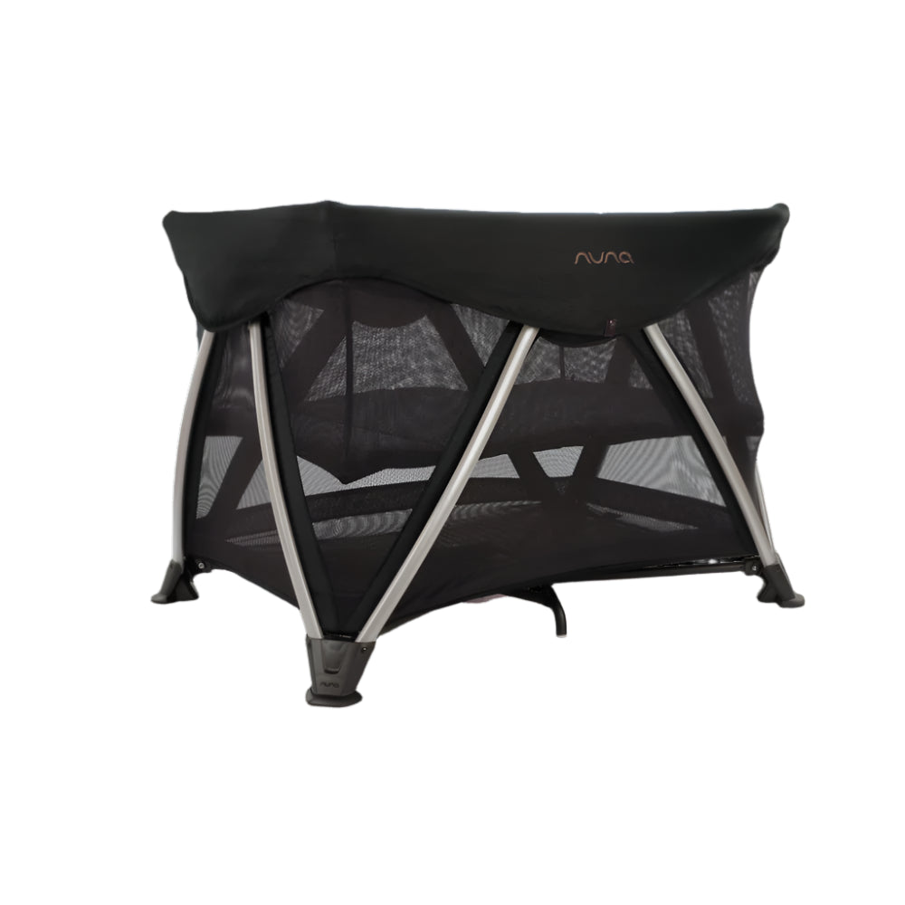 The Nuna travel crib in this image showcases a sleek, modern design with mesh sides for airflow and visibility, supported by sturdy angled legs and a minimalist black canopy top.