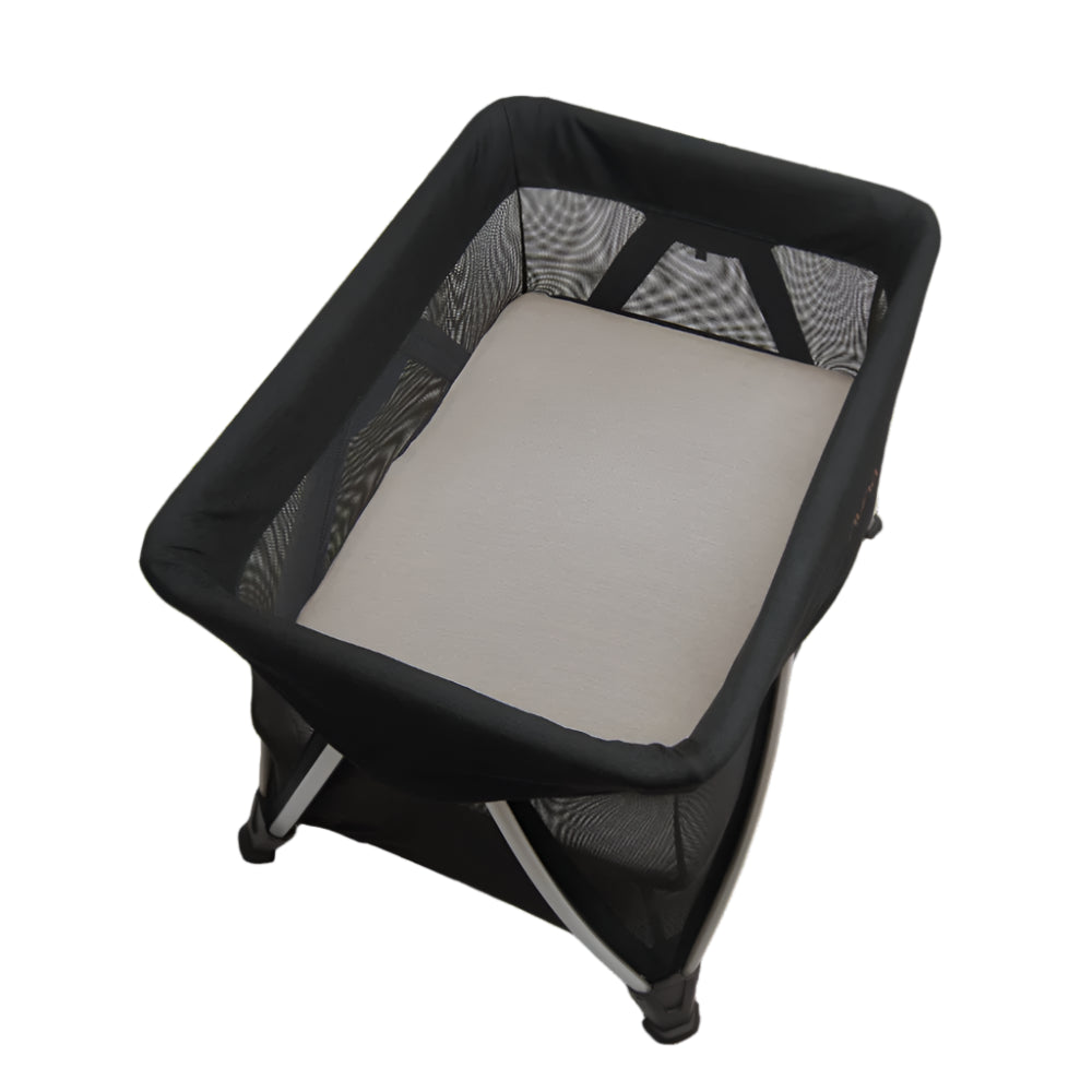 This is a black mesh-sided baby bassinet with a soft beige mattress and sturdy folding frame, designed for portable and breathable infant sleep.