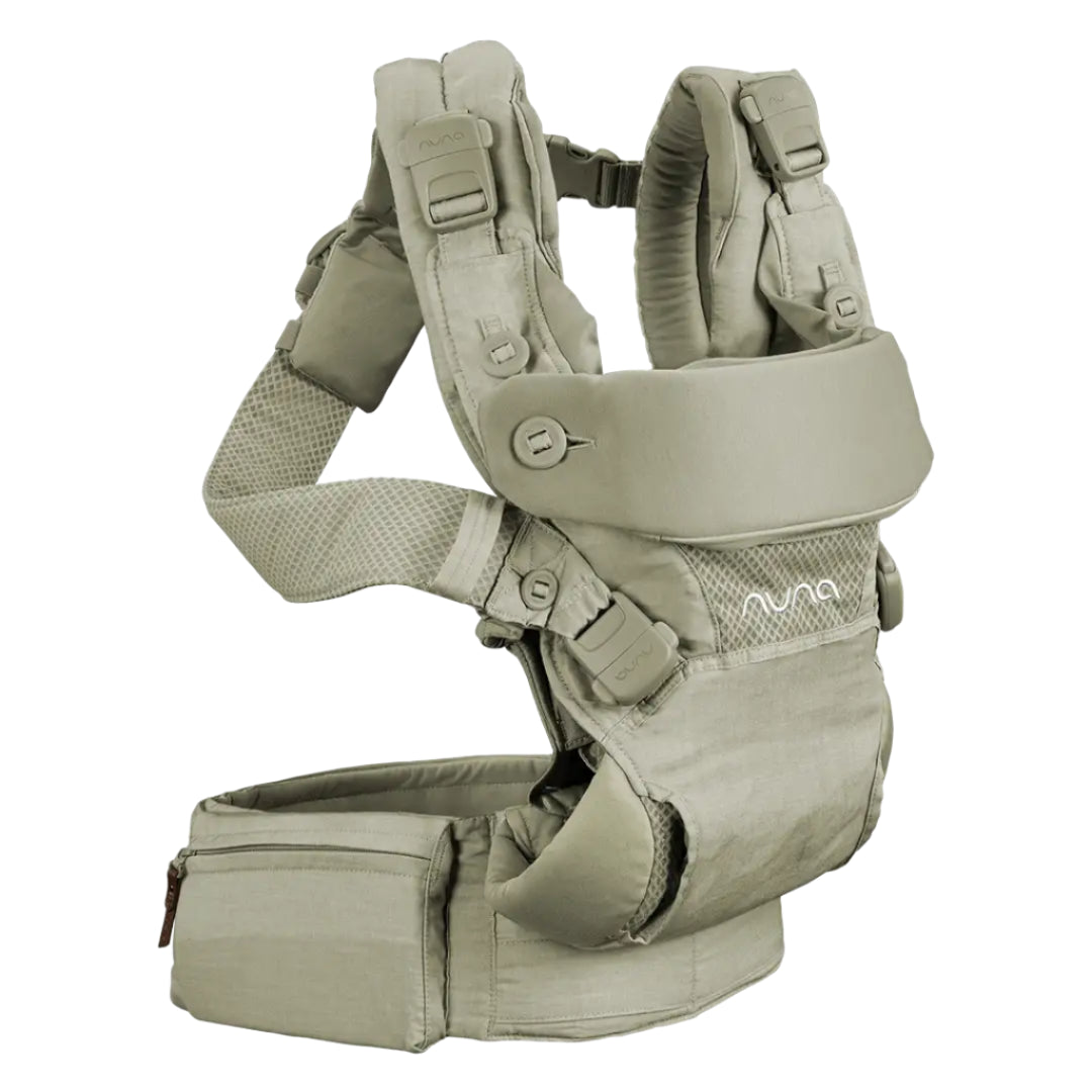 The image shows a beige Nuna baby carrier with padded shoulder straps, mesh ventilation, and a wide waist belt featuring a zippered pocket for storage.