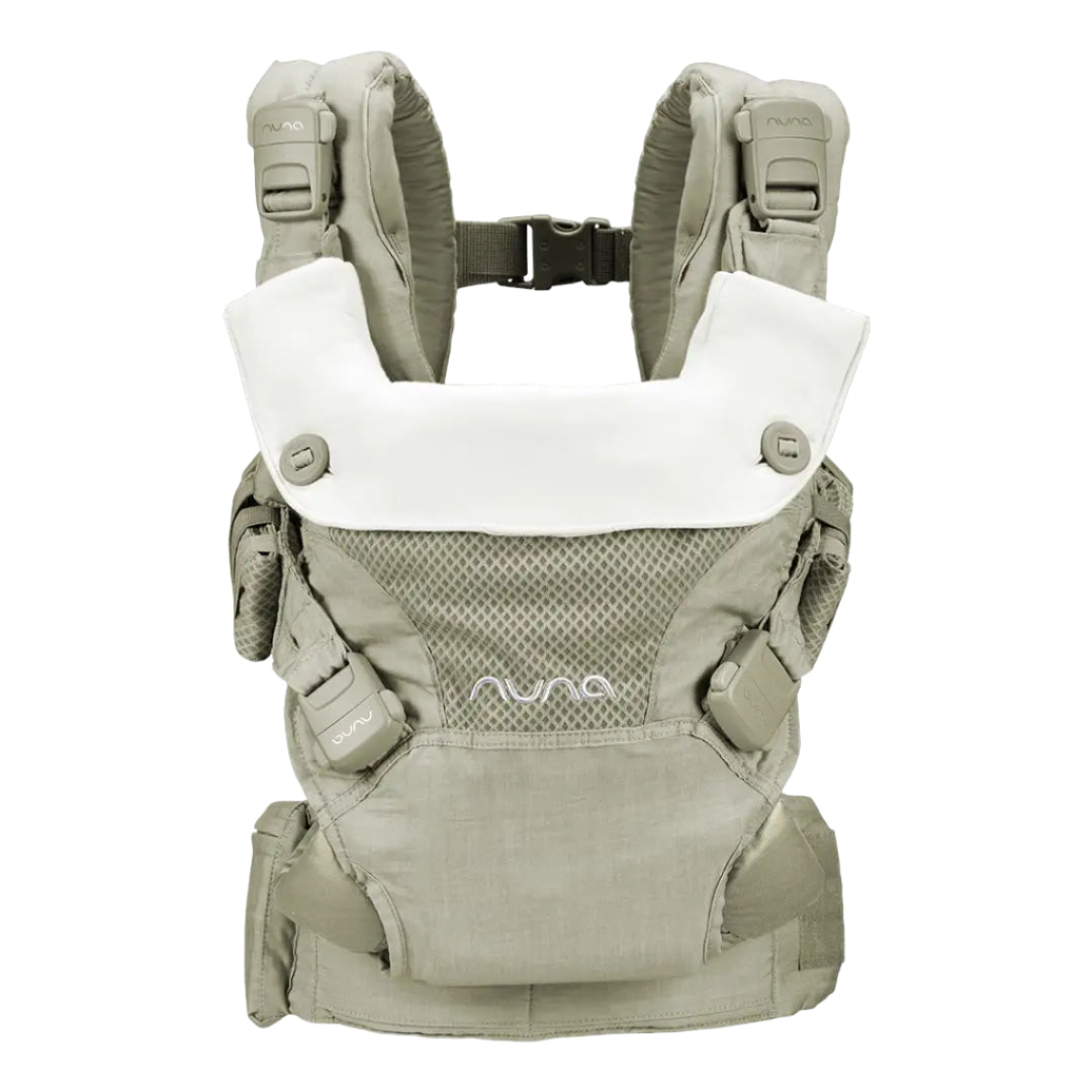The image shows a beige Nuna baby carrier with a white removable head support panel and padded shoulder straps for comfortable babywearing.