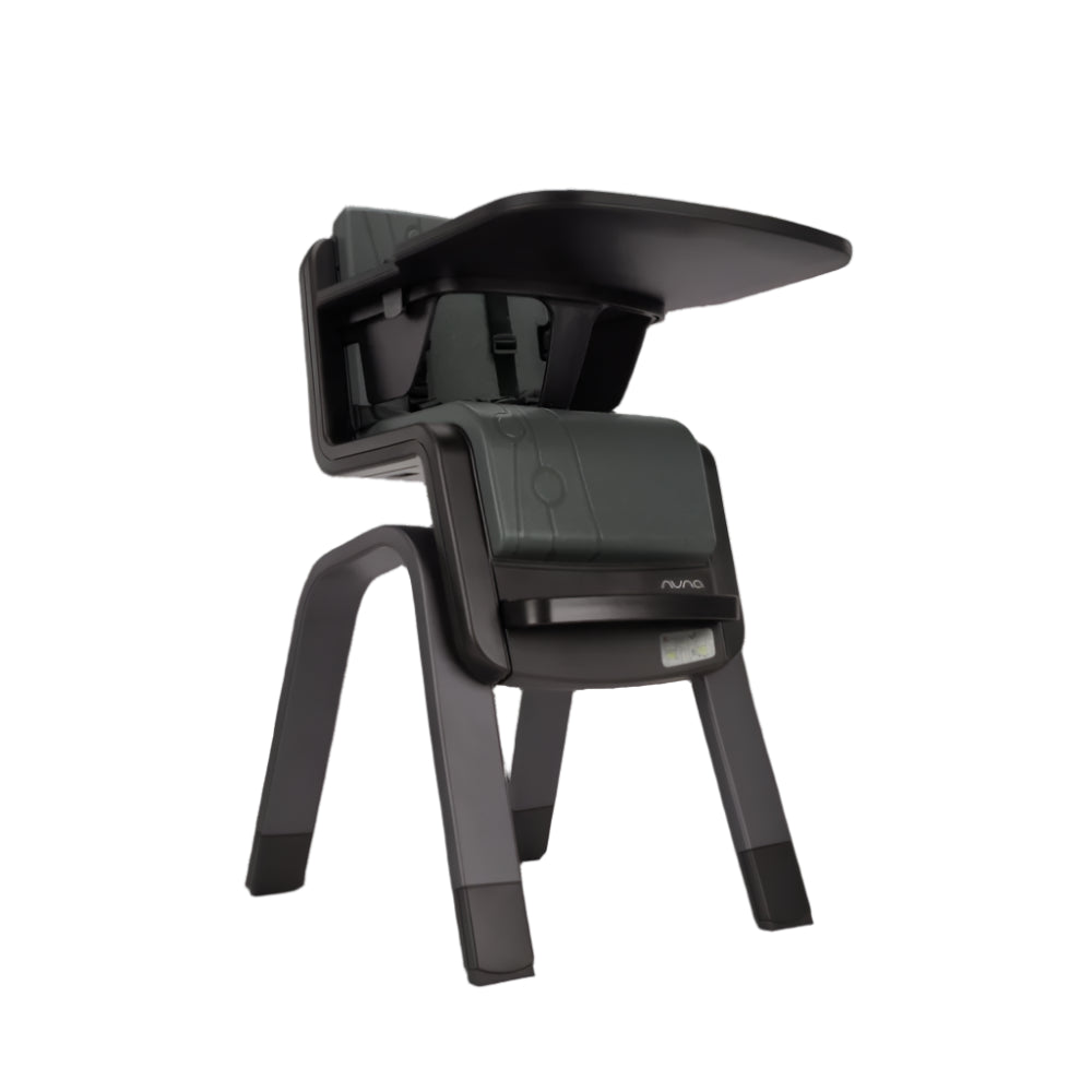 Angled low view of a Nuna high chair in dark green and black, featuring an elevated tray, safety harness, and modern sturdy design for toddler feeding and support.
