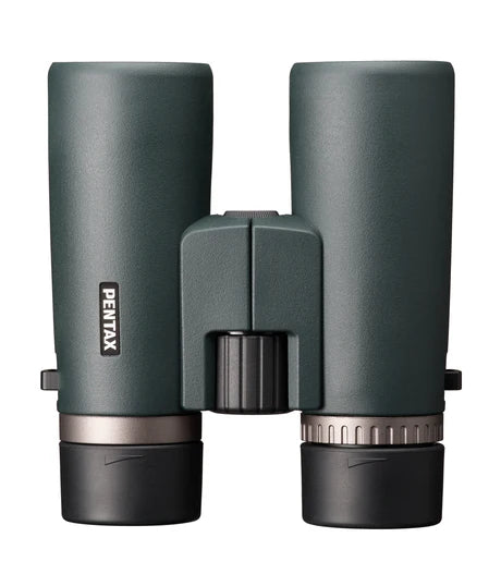 A top-down view of Pentax SD 10x42 ED binoculars. The binoculars have a sleek, ergonomic design with a greenish matte finish. The central focusing wheel is positioned between the two barrels, with the Pentax branding visible on the left barrel. The eyepieces are capped, and the binoculars are designed for comfortable handling and ease of use, emphasizing durability and high-quality optics.