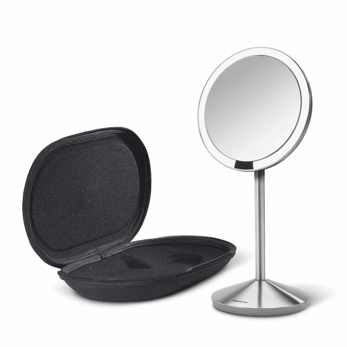 A sleek, circular vanity mirror with a brushed stainless steel stand is displayed alongside an open, black, hard-shell case. The mirror features a thin bezel and is mounted on a slim, conical stand, providing a modern and minimalist appearance. The hard-shell case has a soft interior, designed to securely hold the mirror when not in use, offering both protection and portability. The overall design is stylish and functional, suitable for travel or home use in a contemporary setting.