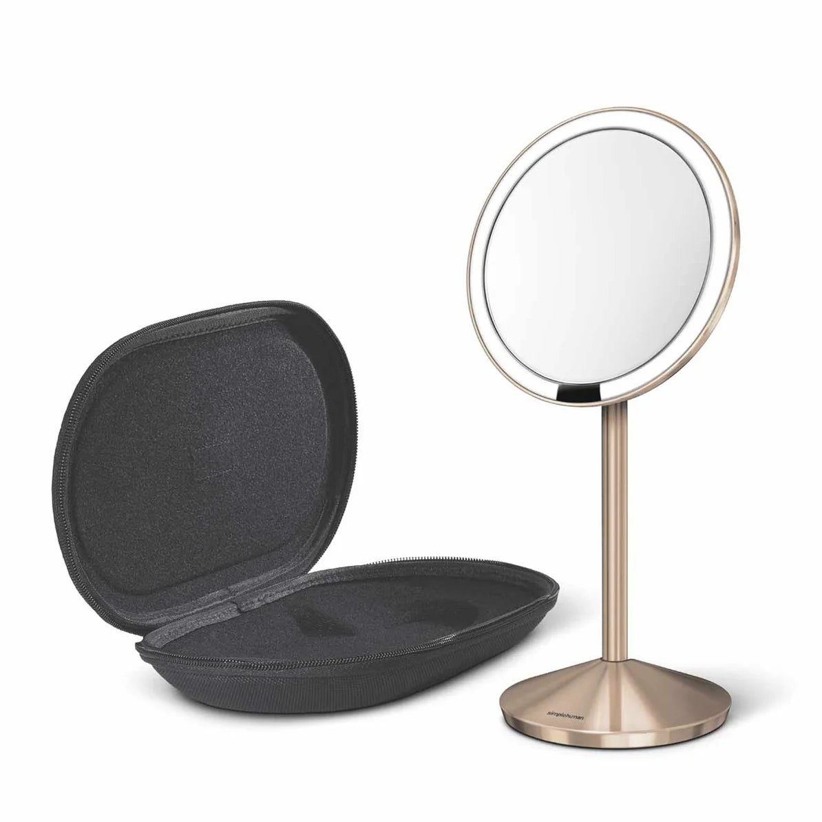 A sleek, modern vanity mirror with a circular design, mounted on a slender metallic stand with a brushed finish. The mirror has a thin bezel and a reflective surface that provides a clear view. Next to the mirror is an open, black, hard-shell case with a soft interior, designed to hold the mirror securely when not in use. The case has a minimalist design, offering protection and portability for the mirror. The overall aesthetic is elegant and functional, suitable for both home and travel use.