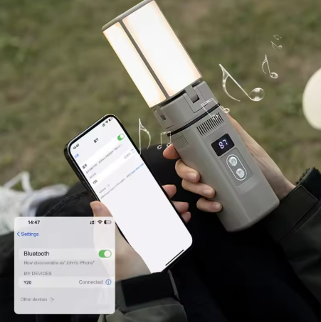 An illuminated portable light held in one hand, connected to a smartphone via Bluetooth, as shown on the phone's screen. Musical notes around the light suggest it doubles as a speaker. The background features an outdoor grassy setting.