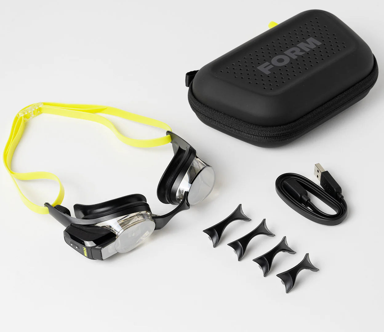 This image displays the FORM Smart Swim Goggles package, including the goggles, a durable carrying case, a USB charging cable, and additional nose bridge pieces for a customizable fit.
