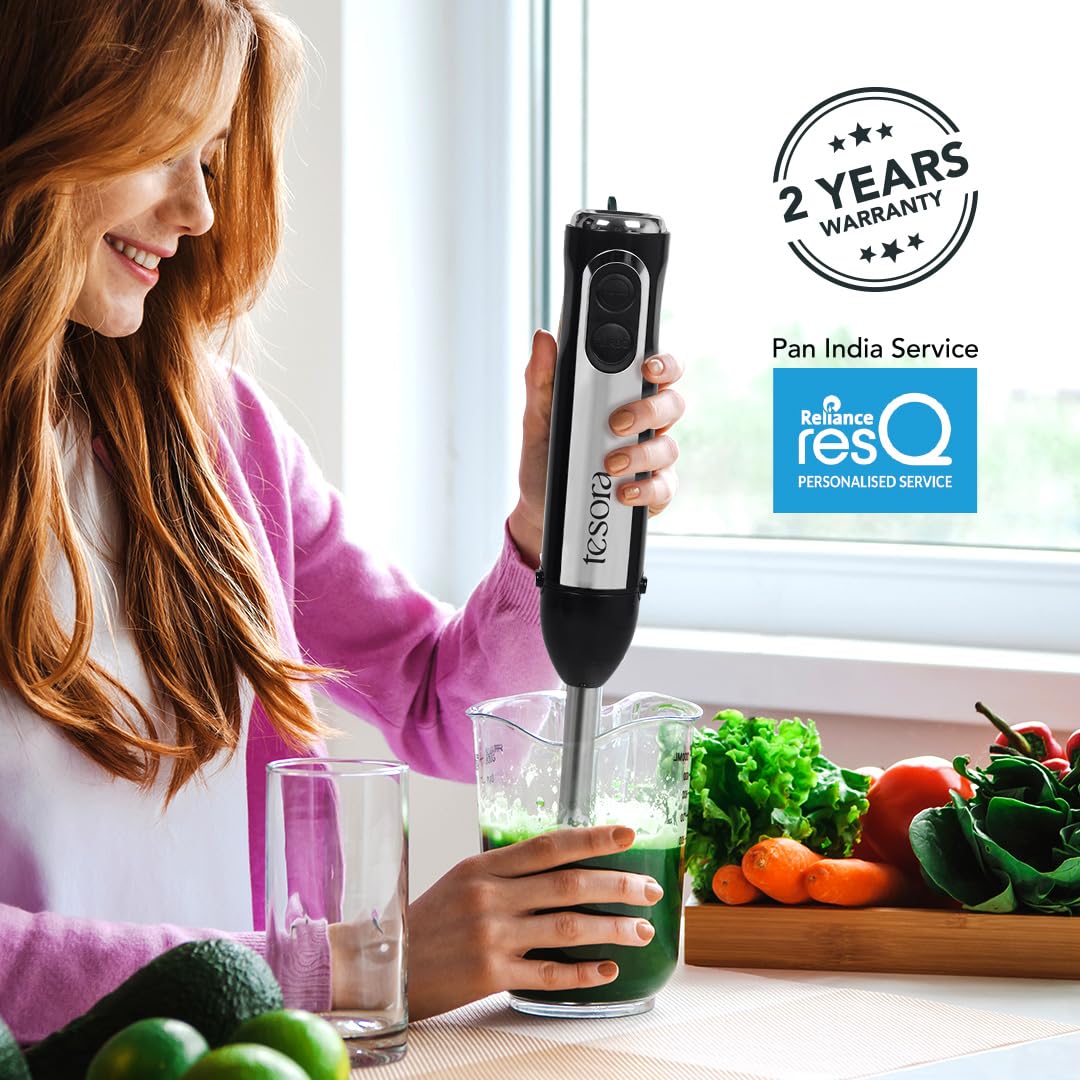 This image features a **Tesora hand blender** in use, blending a green smoothie in a measuring cup. The product highlights include:
- **2 Years Warranty**: Tesora provides a 2-year warranty for the hand blender.
- **Pan India Service**: The brand ensures service across India.
- **Reliance resQ Personalized Service**: The hand blender is supported by Reliance's personalized resQ service for product care.
The scene illustrates the product in a home kitchen setting, emphasizing the blender's efficiency for s
