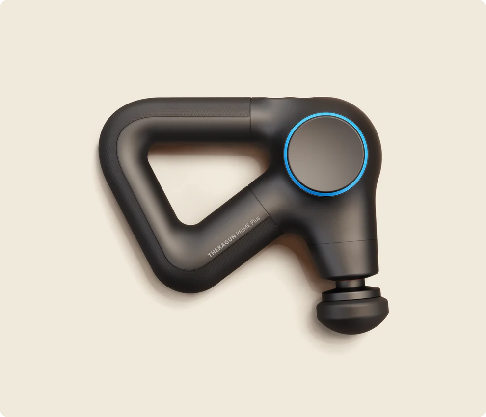 A close-up of the Theragun Prime Plus massage gun, featuring a sleek black design with a triangular ergonomic handle and blue accents. The device has a rounded massage head attachment and is set against a neutral beige background. The text "THERAGUN PRIME Plus" is subtly visible on the handle.