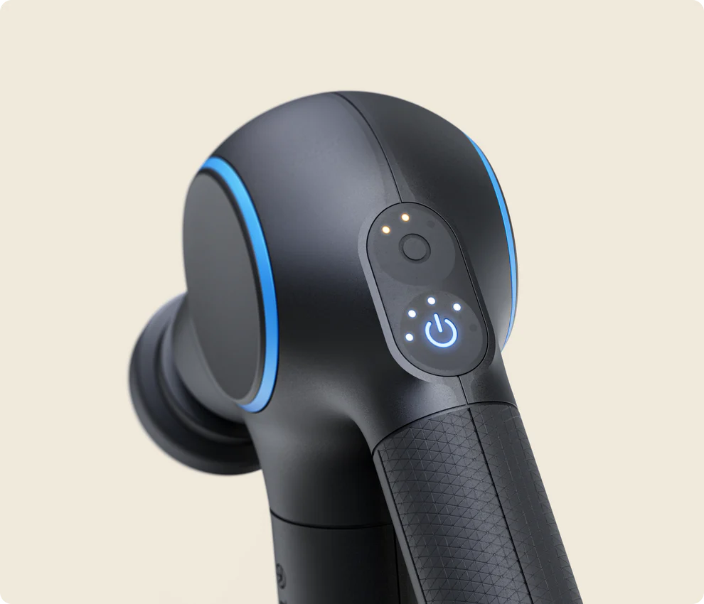 Close-up of a Theragun Pro Plus massage gun, highlighting its control panel. The panel features a power button surrounded by illuminated LED indicators, with additional lights above it. The sleek black design has blue accents, and the handle has a textured grip for ergonomic use. The background is a neutral beige color.