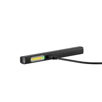 A sleek black LED penlight lying horizontally with a long, narrow LED strip near the top and a USB cable connected to its charging port. The penlight has a rectangular design and a clip on the side for easy attachment. A green charging indicator is visible, showing the penlight is currently being charged.