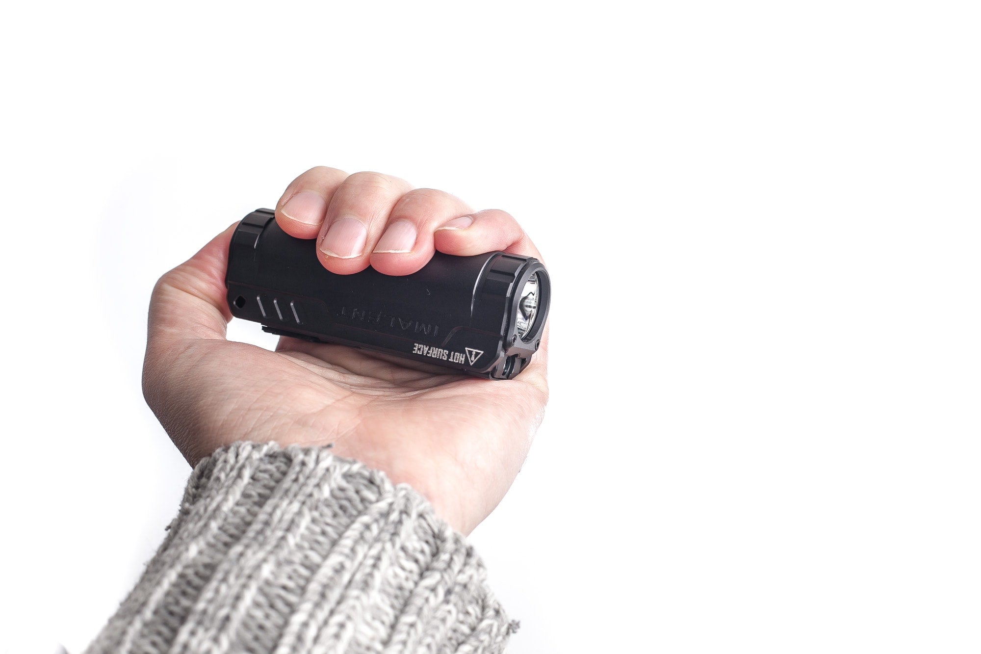 A person holding a compact black flashlight in their hand, demonstrating its small and portable size. The person is wearing a gray knitted sweater.