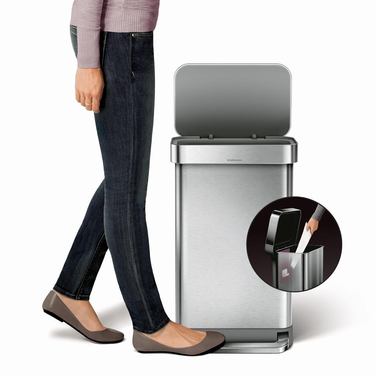Stainless steel trash can with a hands-free foot pedal and an open lid, demonstrating easy waste disposal. A circular inset highlights a built-in compartment for storing extra trash bags. A person walking by showcases the can’s sleek and modern design.