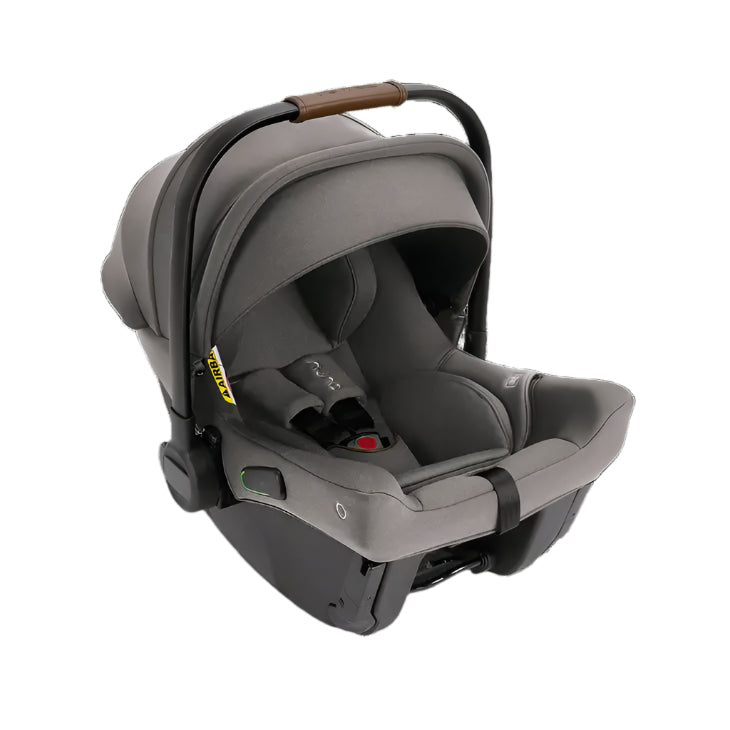 A grey Nuna infant car seat with a brown leatherette handle is shown at an angle, highlighting its contoured design, side-impact protection, and secure five-point harness system.