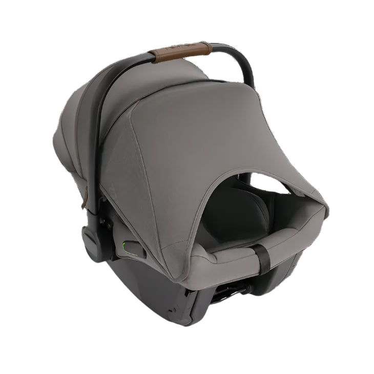 A rear-side view of a Nuna infant car seat in grey, featuring an extended canopy with a mesh peekaboo window, a black and brown leatherette handle, and visible green safety indicator on the base.