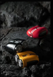 This image features the "Sports Car Shaver" models in three distinct colors: red, black, and yellow, displayed against a rugged, rocky backdrop. The shavers are positioned to emphasize their sleek, aerodynamic designs, reminiscent of sports cars, with metallic accents that add to their premium appearance. The choice of a rugged setting contrasts with the polished look of the shavers, possibly symbolizing their durability and performance, much like high-end sports cars that are built to handle both the fast