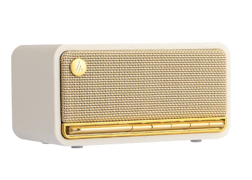 A stylish retro-inspired Bluetooth speaker with a cream-colored body and gold accents. The front panel features a woven fabric grille with a gold control panel at the bottom, consisting of several buttons for adjusting volume, playback, and connectivity. A circular logo emblem is placed on the top left corner of the grille, enhancing its vintage aesthetic. This speaker combines classic design with modern wireless functionality, making it a great addition to any decor.