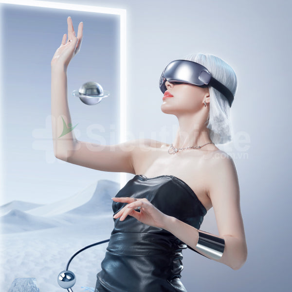A woman with short platinum blonde hair wearing a reflective visor neck massager stands in a futuristic, minimalistic environment. She is dressed in a sleek, strapless black outfit and wears a shiny metallic bracelet on her wrist. One arm is raised gracefully, and she appears to be interacting with a floating metallic sphere in the background. The setting includes a large illuminated frame and smooth, undulating surfaces, enhancing the modern and futuristic aesthetic.