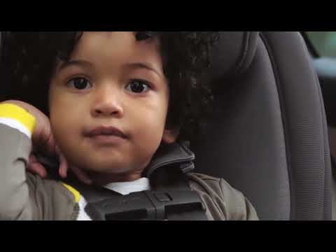 Close-up of a child seated in a Nuna Rava convertible car seat, securely fastened with a five-point harness, as shown in a paused YouTube video by Duck Duck Baby.