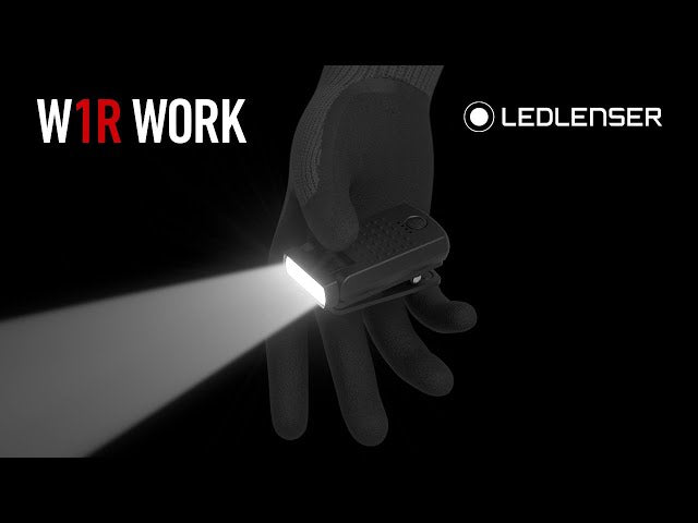 A promotional image for the LED Lenser W1R Work light. The image shows a gloved hand holding the compact black LED light, which is turned on and emitting a bright, focused beam. The text "W1R WORK" and the LED Lenser logo are displayed on the left side of the image. The background is dark, highlighting the brightness of the LED light.