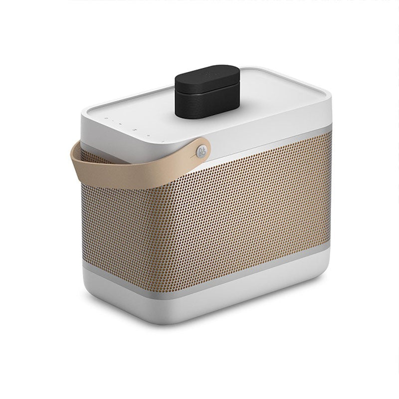 This image features a **Bang & Olufsen (B&O) portable speaker**, showcasing its sleek and premium design. The speaker body is primarily light grey with a **golden-honeycomb grille** that wraps around the sides, enhancing its aesthetic appeal. A **leather strap** is attached to the side, adding a touch of elegance and portability. On the top of the speaker, there is a **black accessory or attachment**, which could be a part of the speaker's modular design or a protective cover. The minimalistic buttons on th